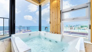 Une grande baignoire offrant une vue sur la mer et le paysage urbain grâce à de larges fenêtres.