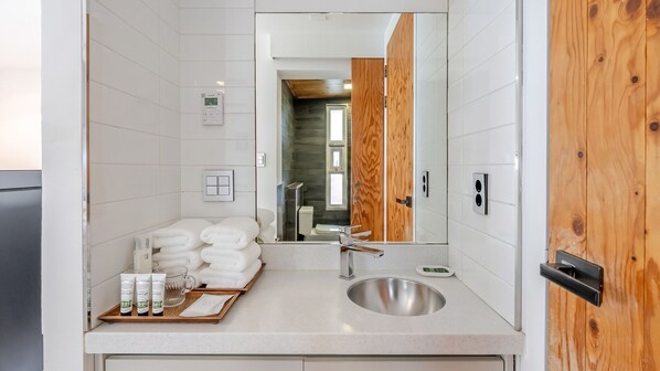 A modern bathroom with a wooden door, a sink, a mirror, and a tray with toiletries.