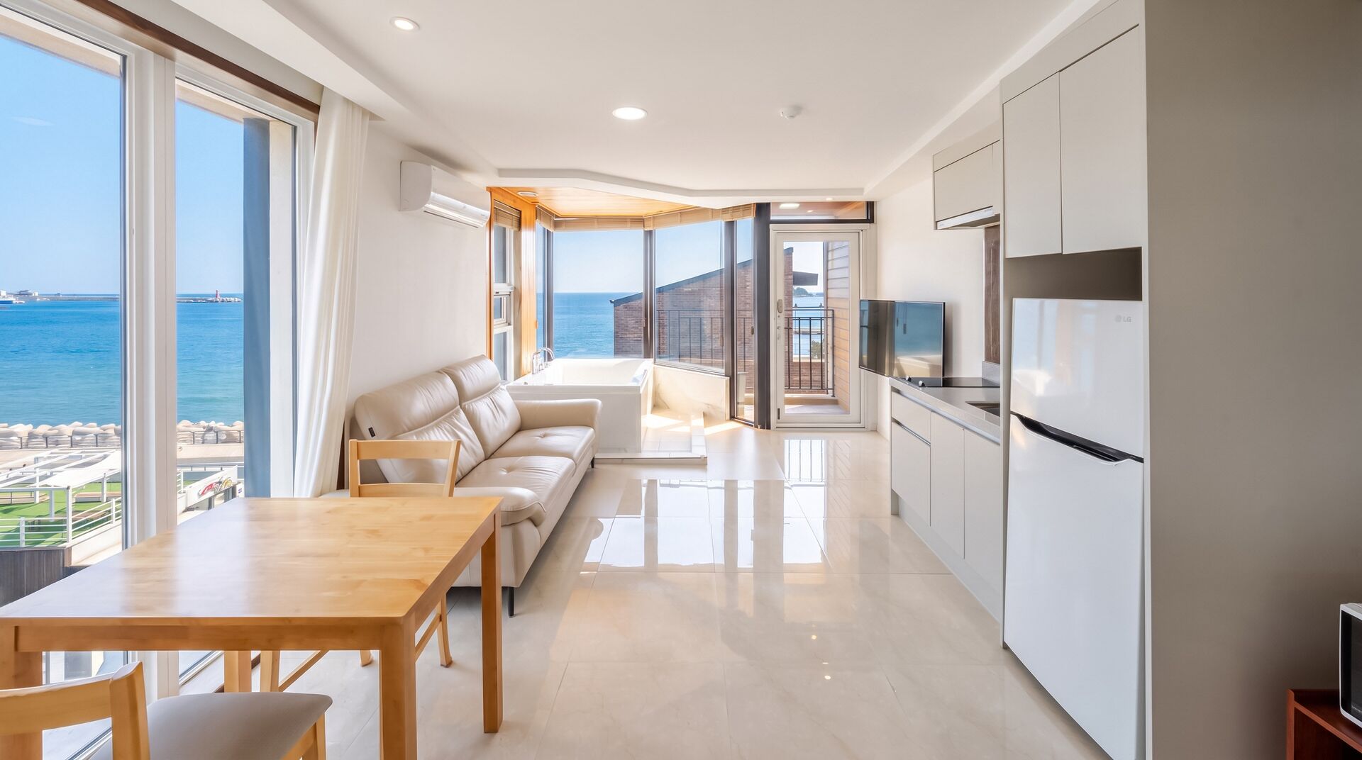A modern kitchen with a view of the sea, a dining area with a table and chairs, and a living space with a sofa and a TV.