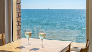 Una mesa con dos copas de vino blanco, un muro de piedra y vista al mar.