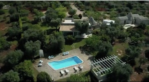 Oversigtsbillede af en ejendom med swimmingpool, liggestole og en pergola.