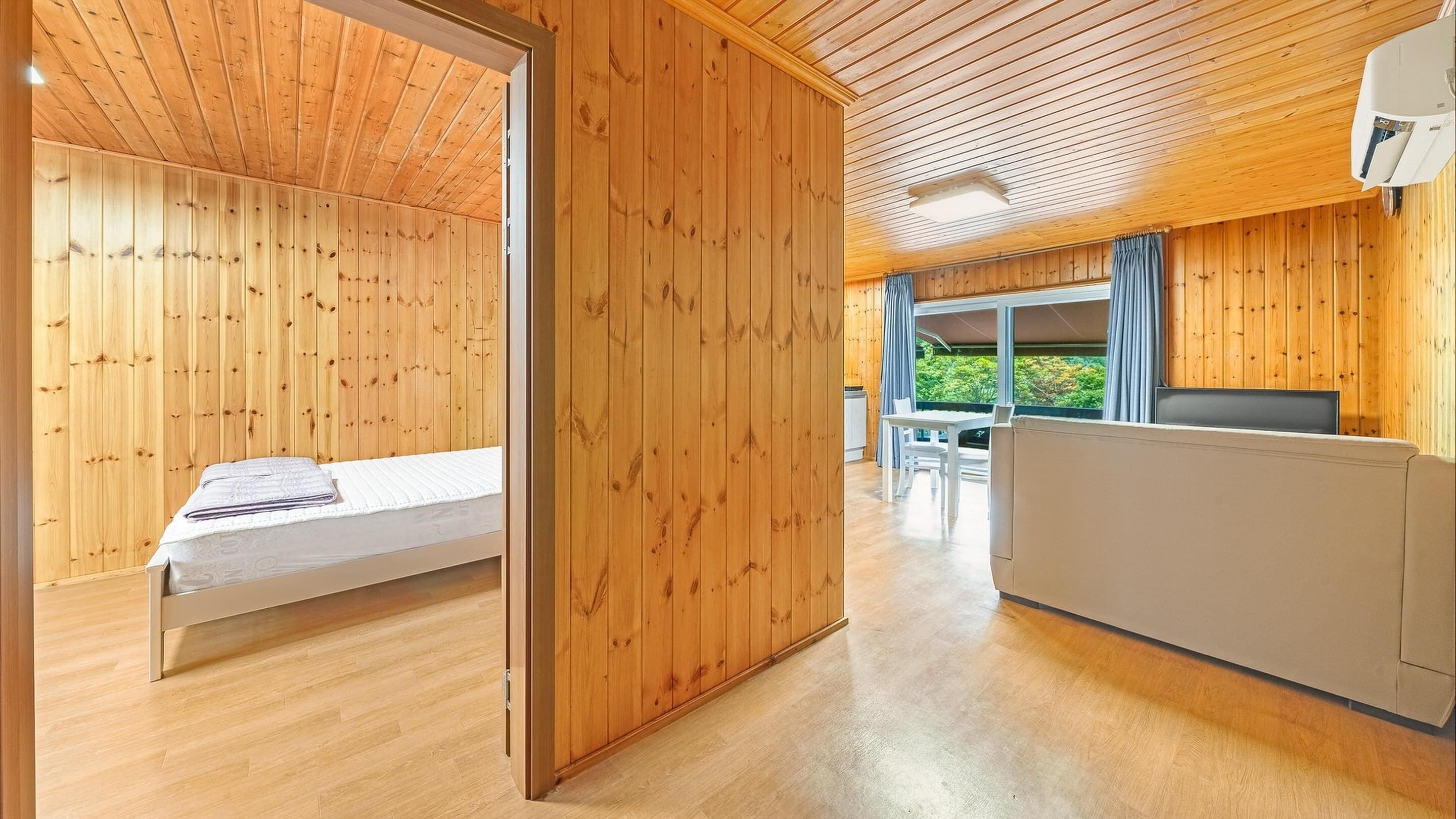 Une cabane en bois comprenant un lit, un coin repas et donnant sur un paysage verdoyant.