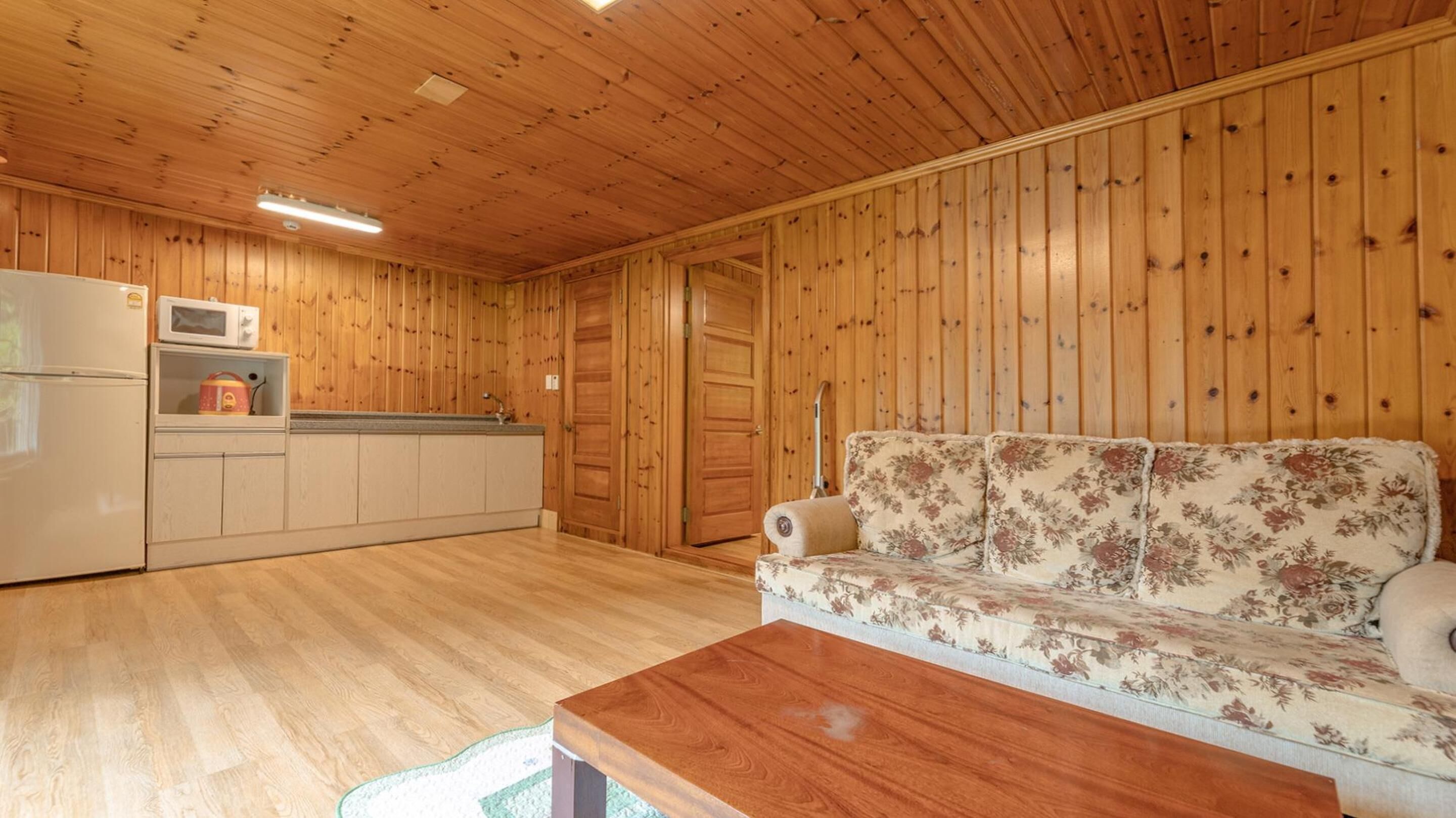 Ein Zimmer mit Holzwandverkleidung, einer Küchenzeile, einer Couch und einem Holztisch.