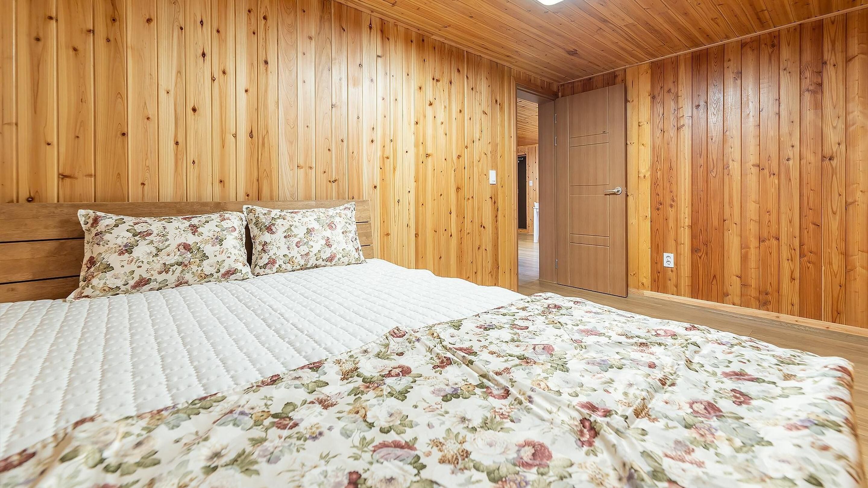 Un dormitorio con paneles de madera, una cama, ropa de cama floral y un armario.