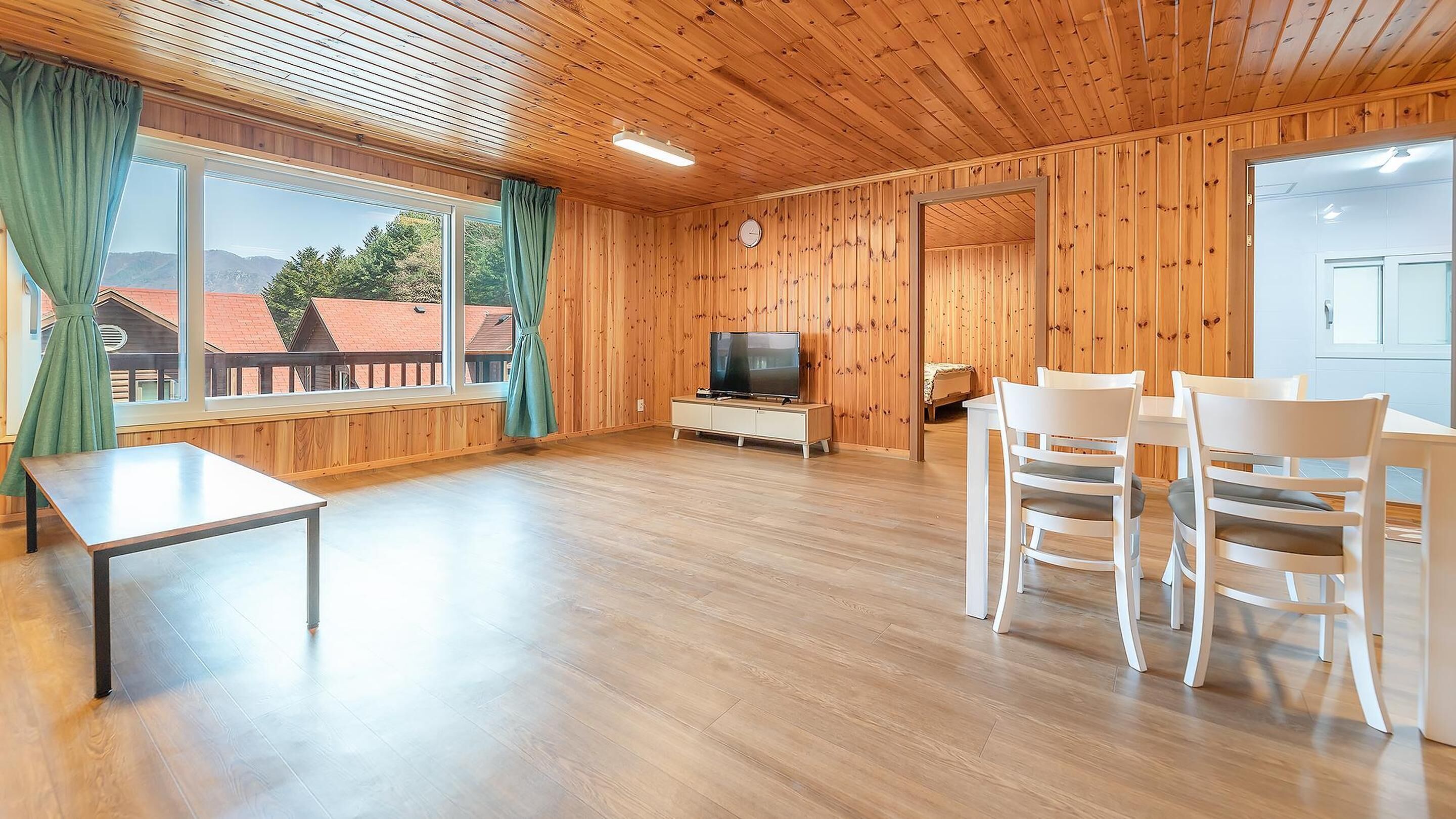 Una habitación con paneles de madera, un televisor, una mesa de comedor con sillas y una cama al fondo.