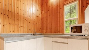 A kitchen with wooden walls, a window, a sink, and a microwave.