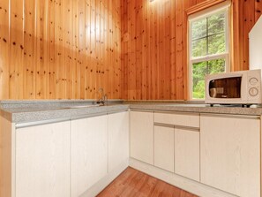 A kitchen with wooden walls, a window, a sink, and a microwave.