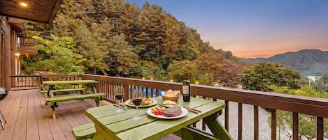 Una terraza de madera con mesas de picnic, una botella de vino y un cesto de pan.