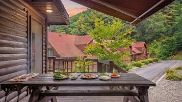 Une terrasse en bois avec une table dressée pour un repas, entourée d’une colline boisée.