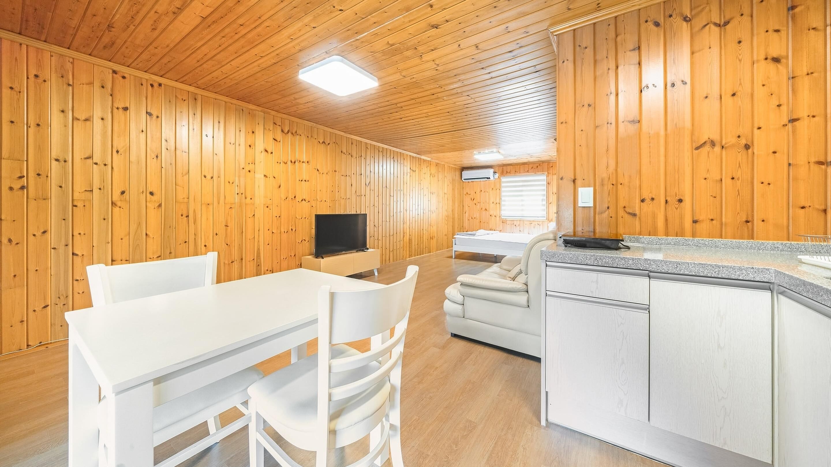A modern cabin interior with a dining area, a sofa, a kitchen with a granite countertop, and wooden walls.