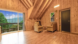 A spacious room with wooden walls and a balcony overlooking a mountainous landscape.