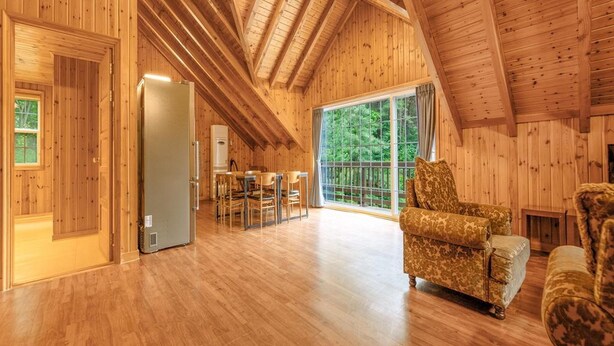 A spacious wooden interior with a high ceiling, a dining area, and a large window offering a view of the outdoors.