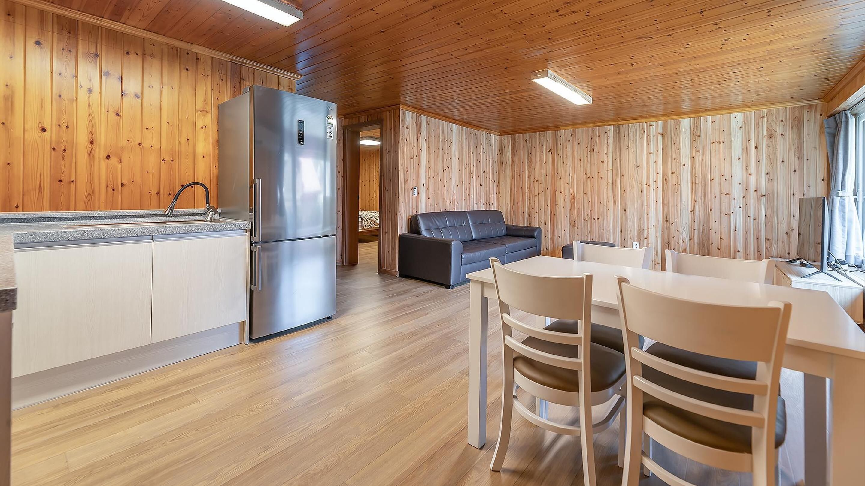 Una cocina moderna con refrigerador de acero inoxidable, paredes de madera y un comedor con sillas blancas y una mesa.