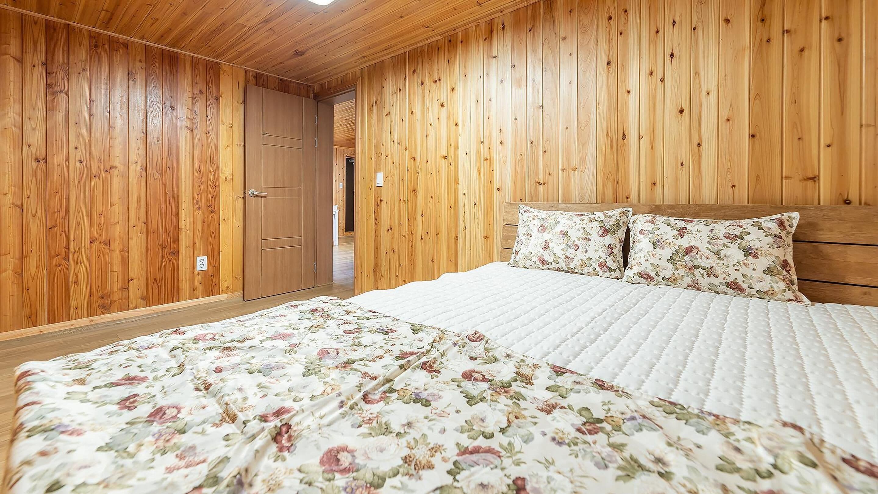 A bedroom with wooden walls, a bed with floral bedding, and a wooden door.