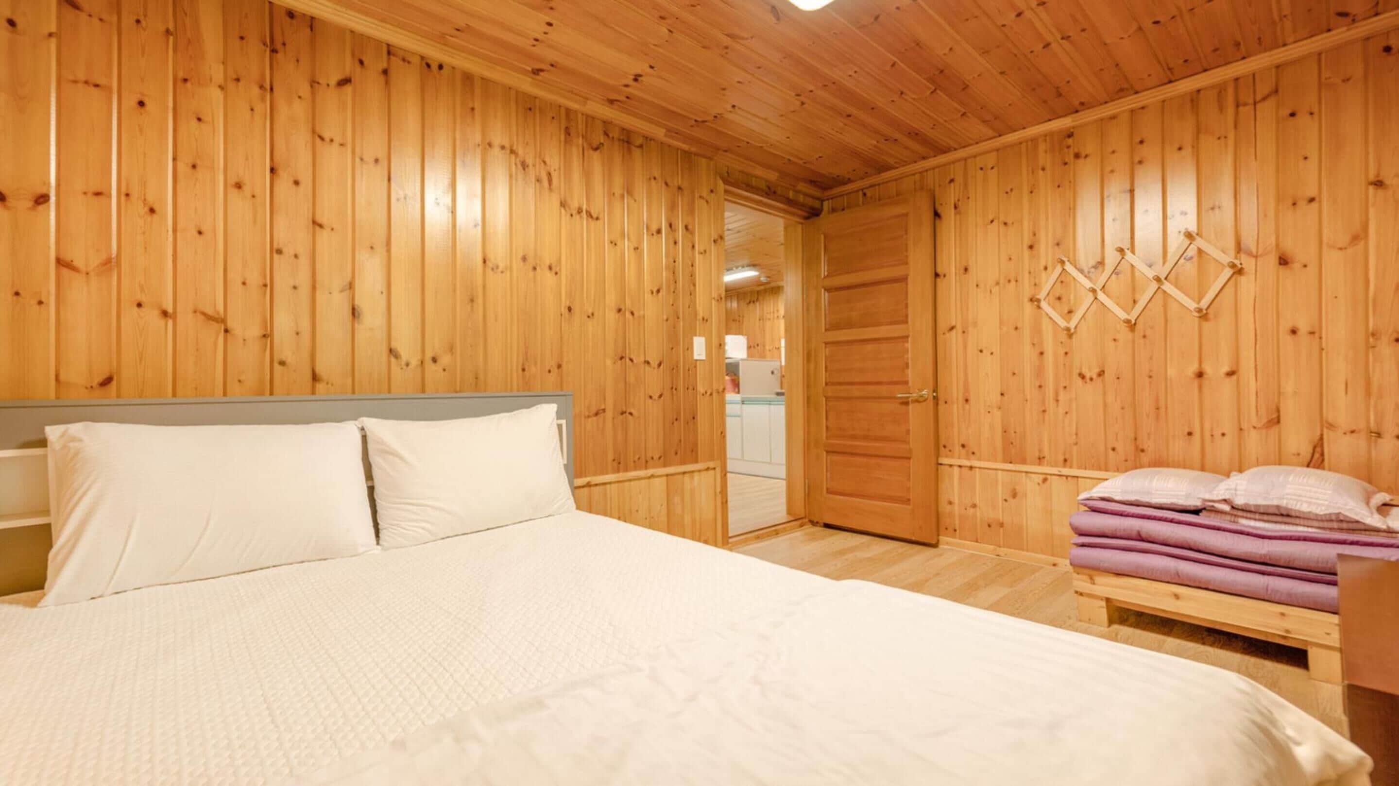 A wooden room with a bed, a wooden wardrobe, and a small table with folded towels.