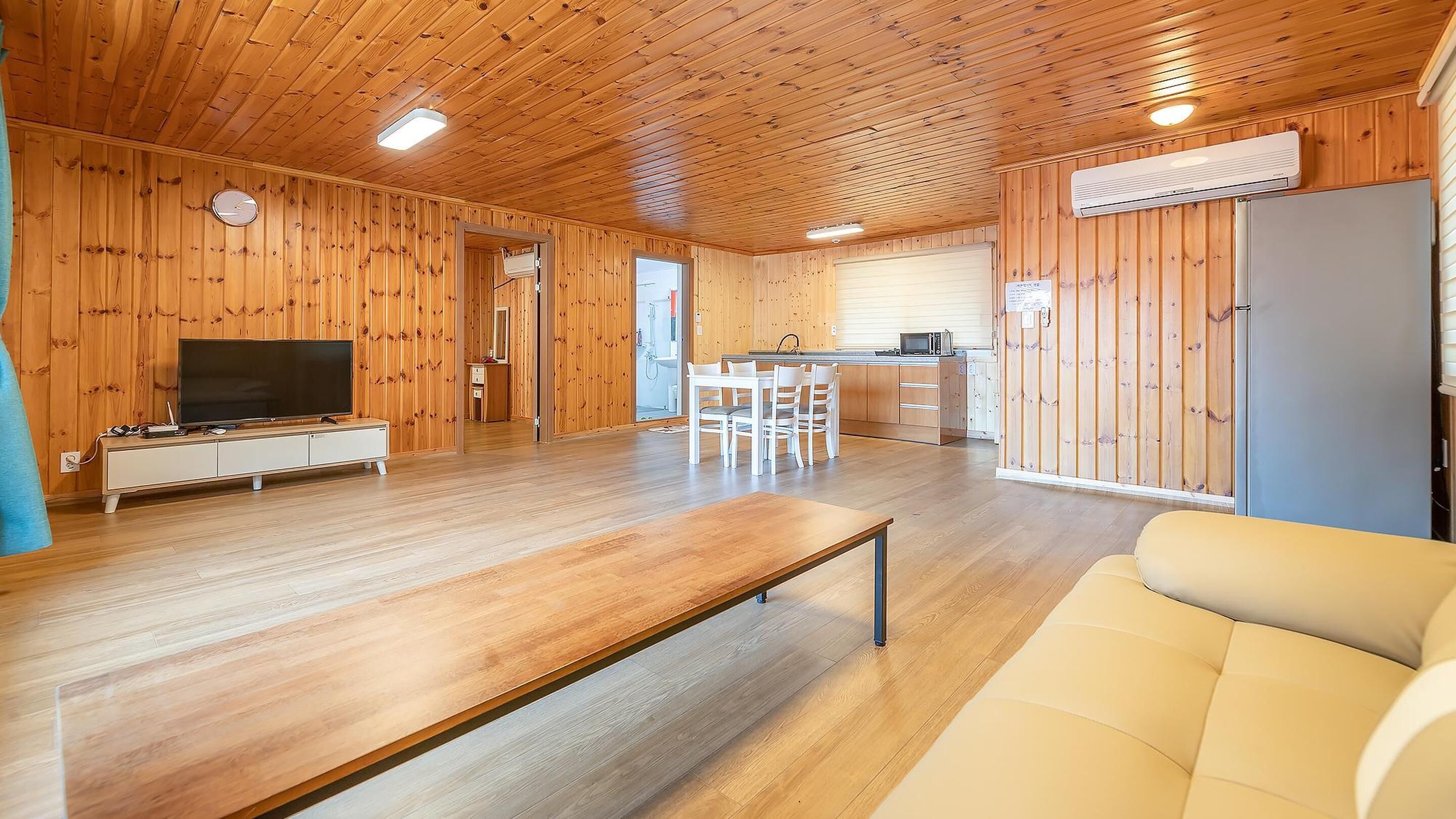 Een kamer met houten lambrisering, een televisie, een eettafel en een bank.