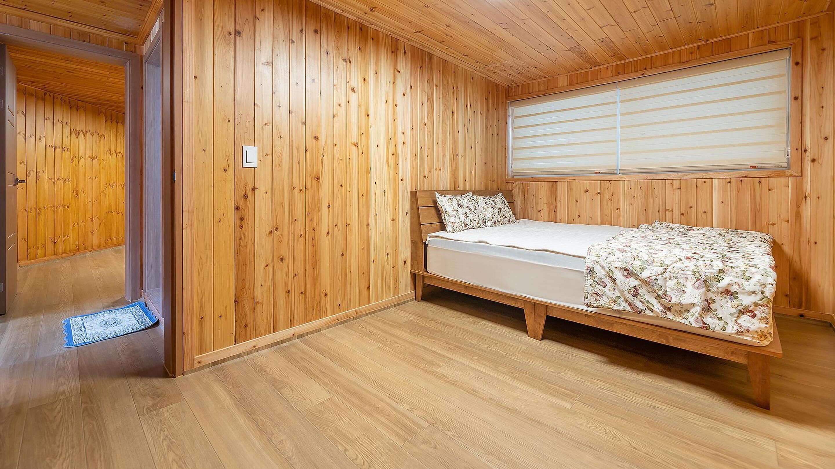 A wooden-paneled room with a bed, a window with blinds, and a door.