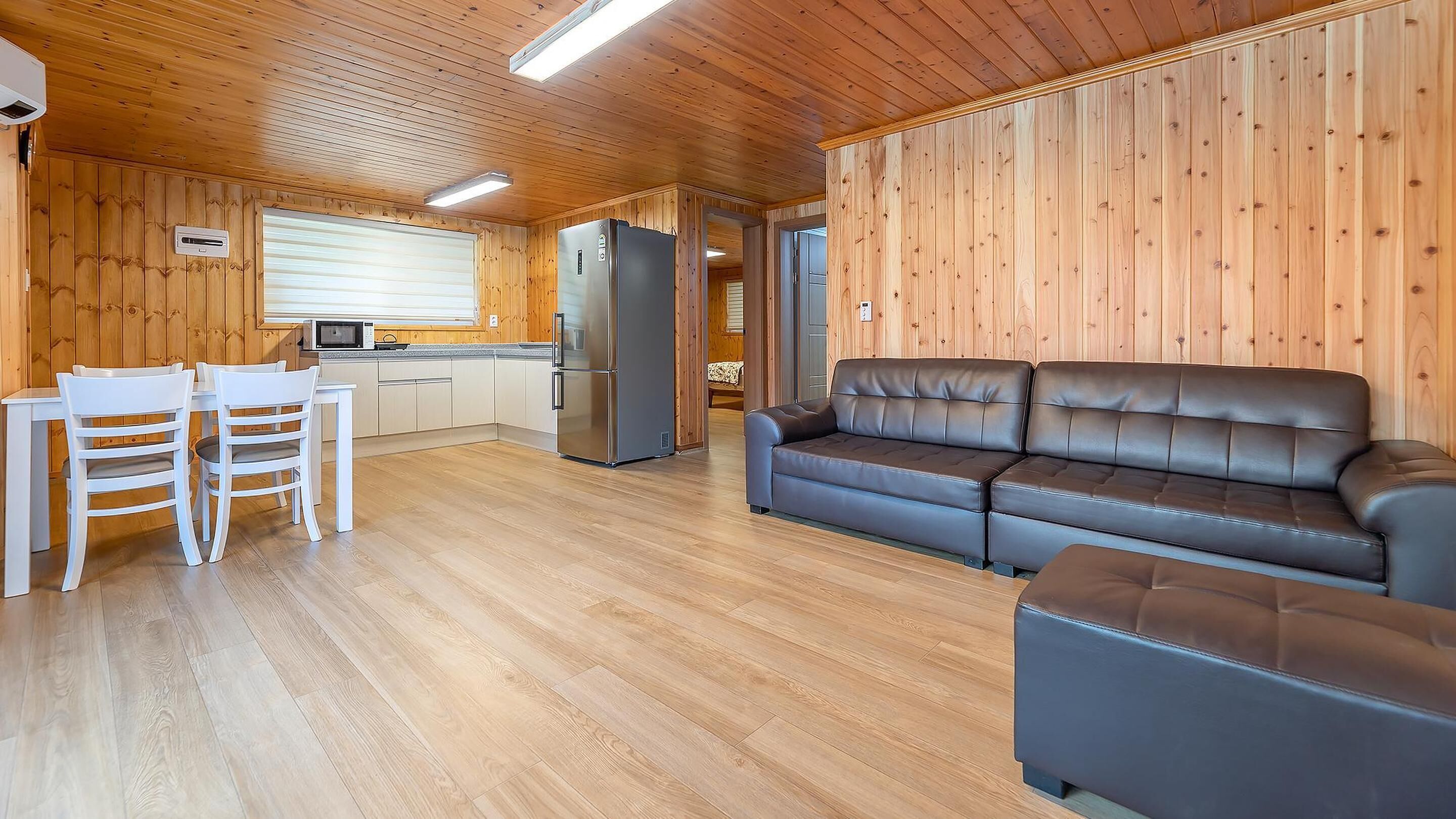 Interior acogedor de una cabaña con detalles de madera, una kitchenette, un comedor con mesa y sillas, y un sofá.