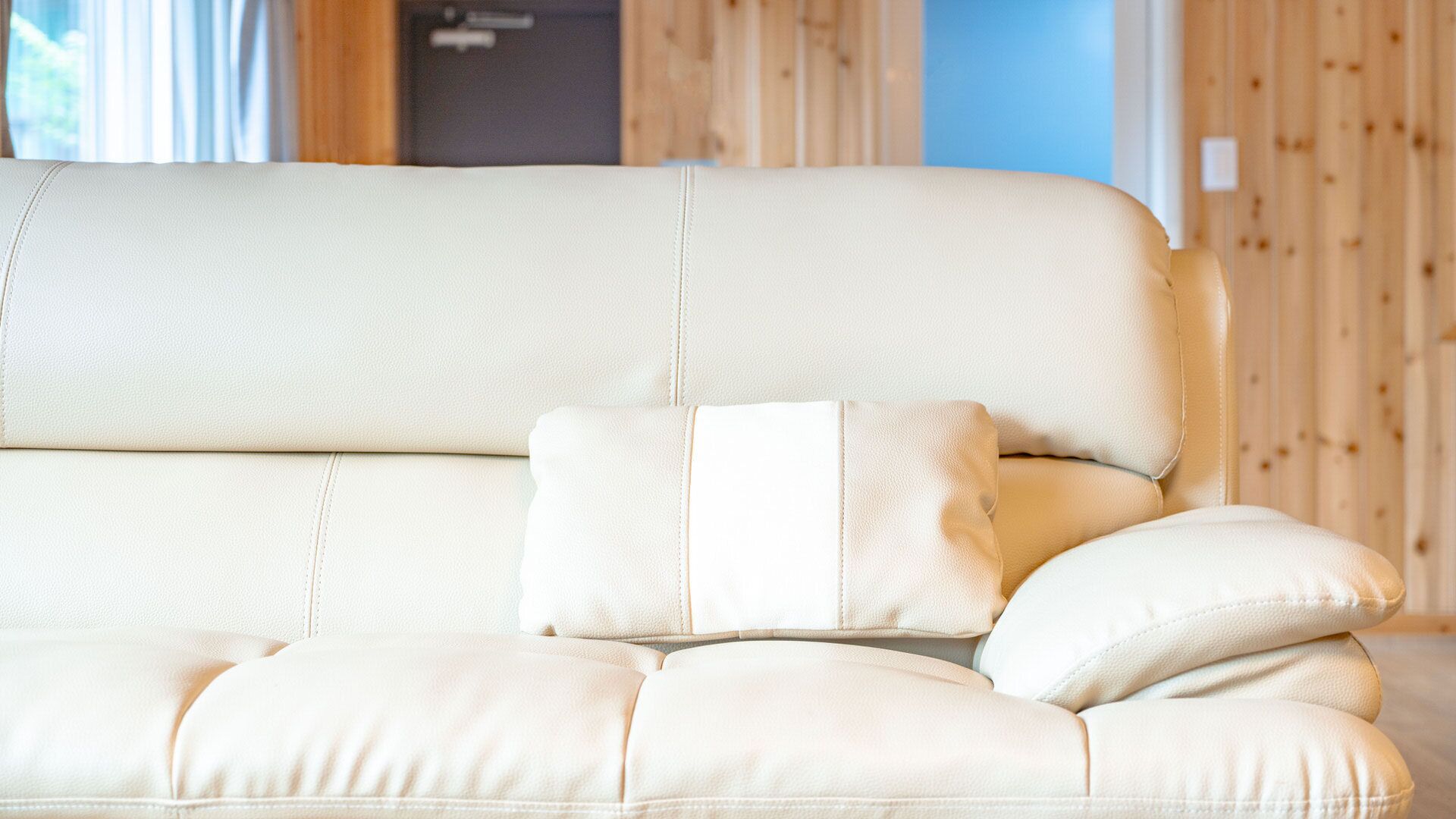 A beige sofa with a matching cushion in a room with wooden paneling.