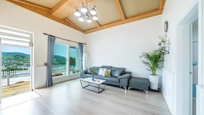 Amplia sala de estar con un gran ventanal, un sofá gris, una mesa de centro y un techo con vigas de madera y un candelabro.