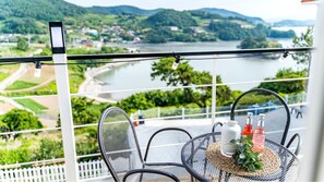 A balcony with a table set for two, overlooking a river and hills.