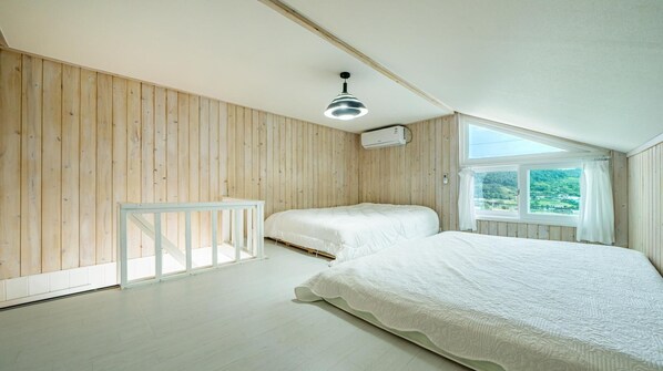 A bedroom with two beds, wooden walls, a skylight, and a white railing.