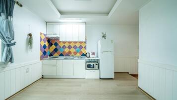 A compact kitchen with white cabinets, a colorful diamond-patterned backsplash, a microwave, a kettle, and a refrigerator.