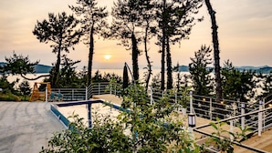 Zona de piscina con muelle de madera, barandilla metálica y vista al atardecer sobre el agua.