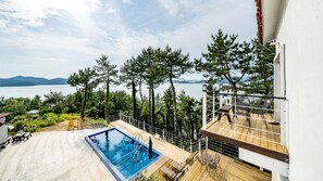A rooftop pool with a view of a lake and mountains, surrounded by trees and a white building.