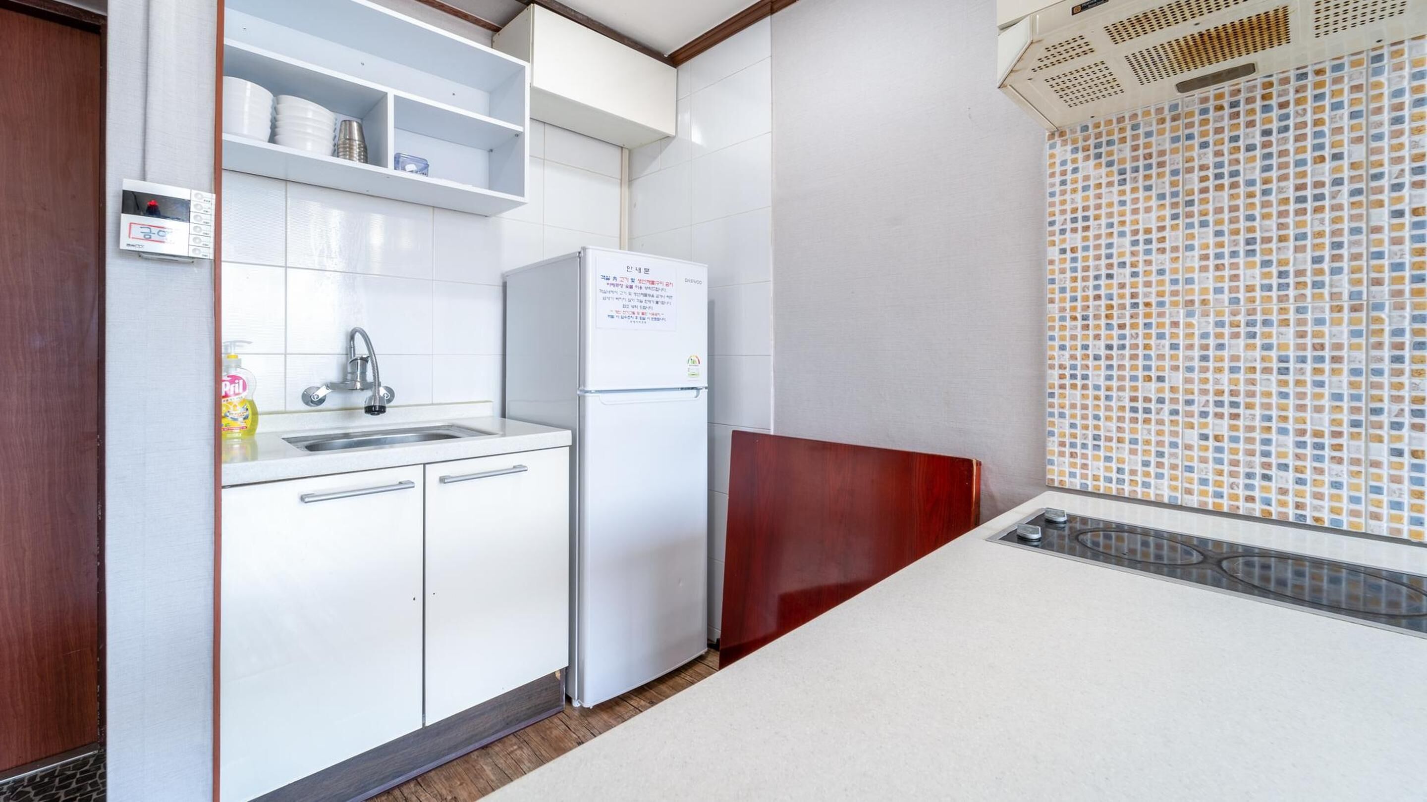 A compact kitchen with white cabinets, a stainless steel sink, a refrigerator, and a tiled backsplash.