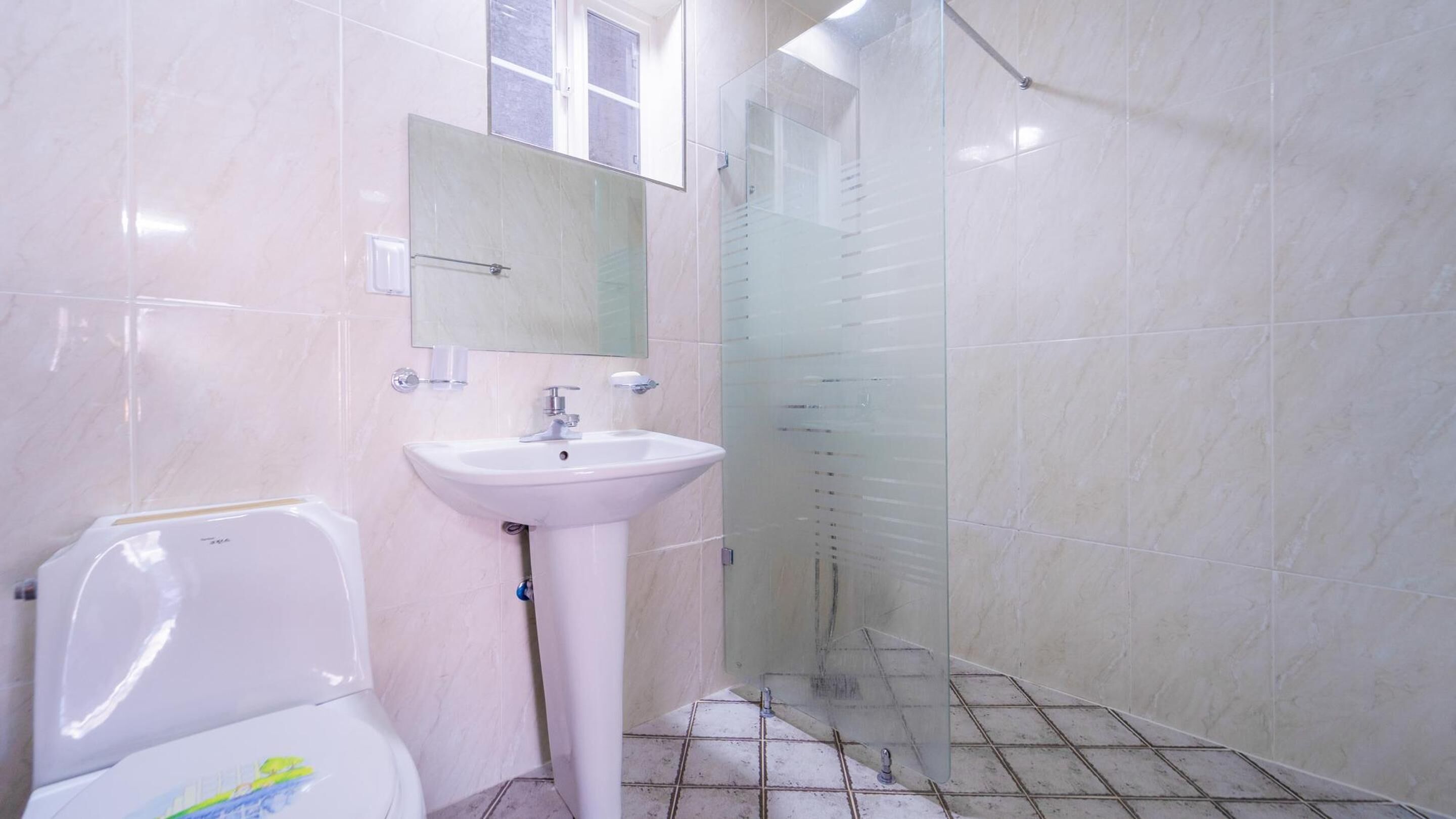 A bathroom with a toilet, sink, and glass shower enclosure.