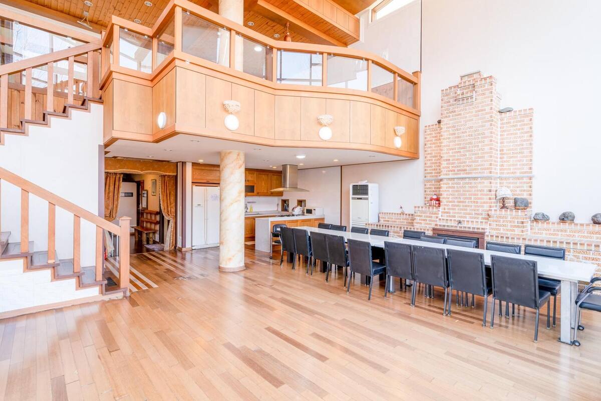 Un intérieur spacieux à plusieurs niveaux, doté d’un escalier en bois, d’un coin cuisine et d’un espace repas avec plusieurs chaises.