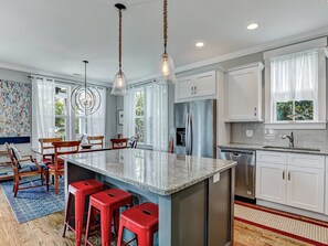 Une cuisine moderne dotée d’un grand îlot central, d’appareils électroménagers en acier inoxydable et d’un coin repas avec des chaises en bois et un tapis bleu.