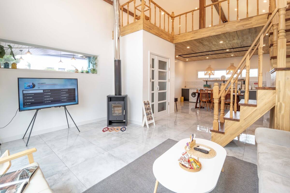 En rummelig opholdsstue med en moderne pejs, et spiseområde og en trappe til en etage ovenpå.