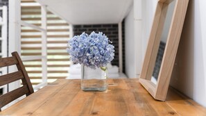 A wooden table with a clear glass vase containing blue flowers, a wooden chair, and a picture frame on the right side.