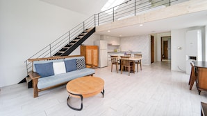 A spacious living area with a sofa, round coffee table, dining table with chairs, a kitchen, and a staircase.