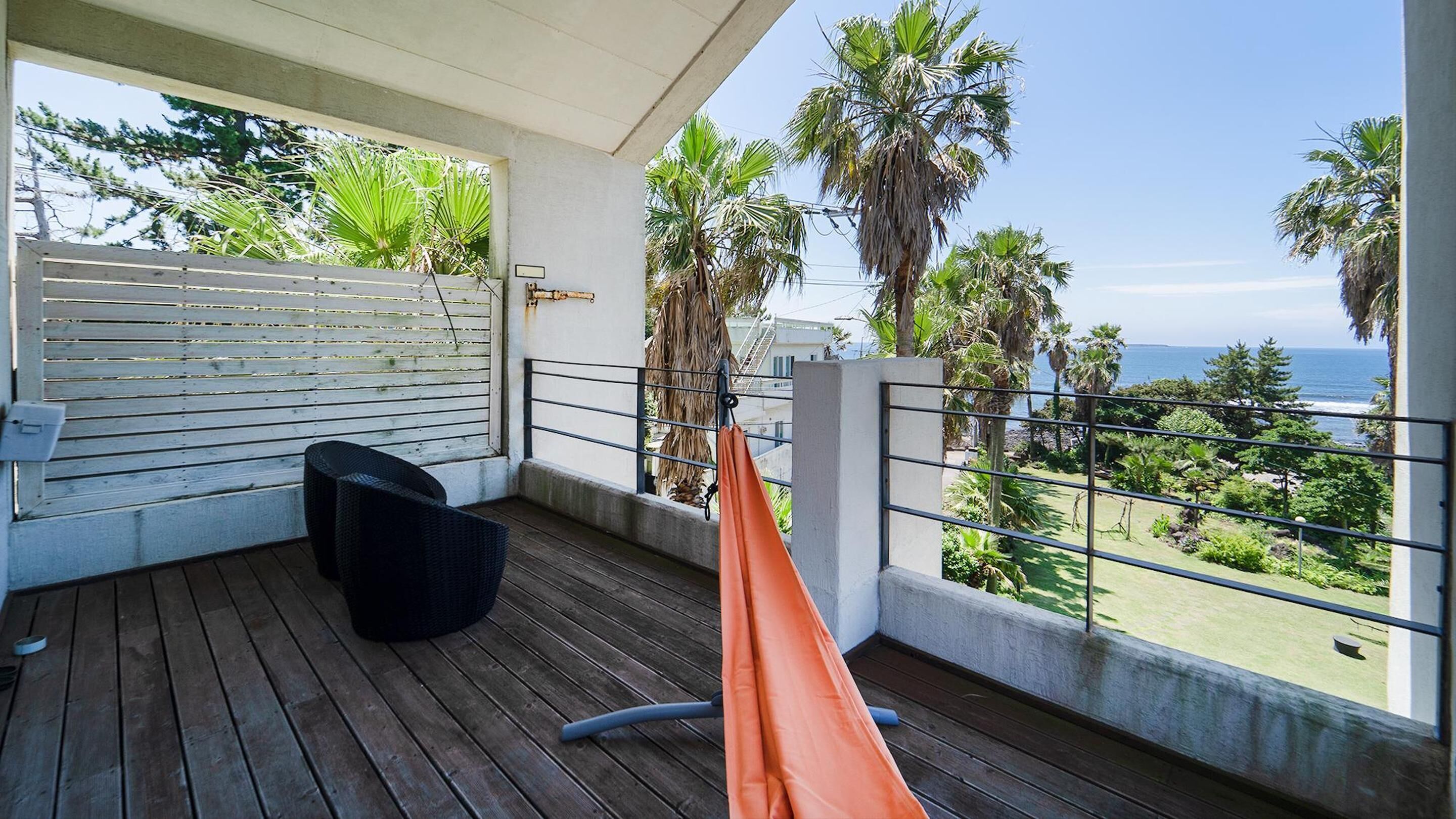 A balcony with a wooden floor, a black wicker chair, and an orange hammock.