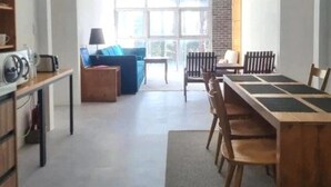 A modern living room with a sofa, a coffee table, and a dining table with chairs. There is a window with a view of trees and a brick wall.
