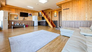 Ein gemütliches Wohnzimmer mit einer Couch, einem großen Teppich, Holzwänden, einem Fernseher und einer Küchenzeile mit einer Treppe.