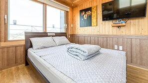 A bedroom with a bed, wooden walls, a window, and a television on the wall.
