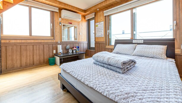 Ein Schlafzimmer mit einem großen Bett, Holzwänden, einem kleinen Schreibtisch und einem Fenster.