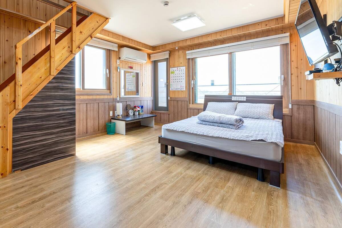Ein Schlafzimmer mit einer Holztreppe, einem Bett, einem Schreibtisch und großen Fenstern.