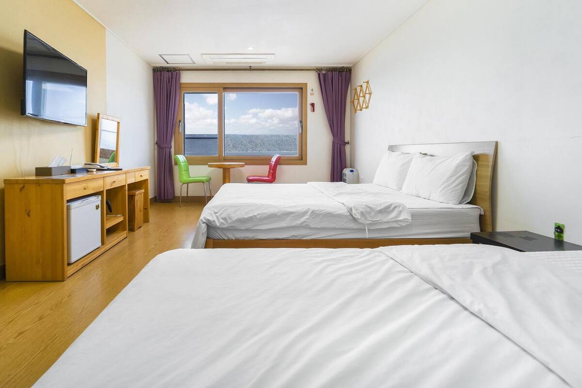 Habitación de hotel con dos camas, un escritorio con computadora, un refrigerador pequeño y un televisor.
