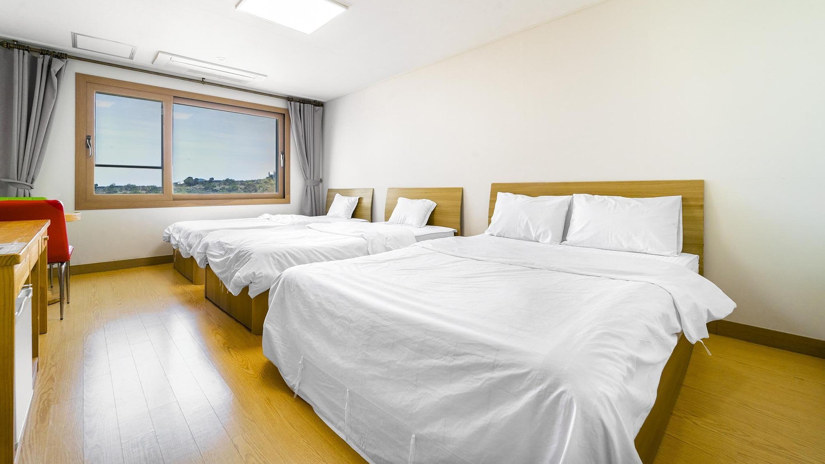 Habitación de hotel con dos camas individuales, un escritorio de madera y una ventana con vistas al paisaje.