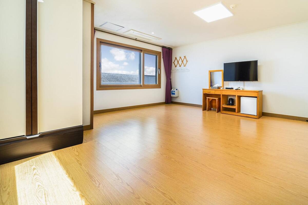 Amplia habitación con piso de madera, un gran ventanal con vistas, televisor de pantalla plana y un pequeño escritorio de madera con silla.