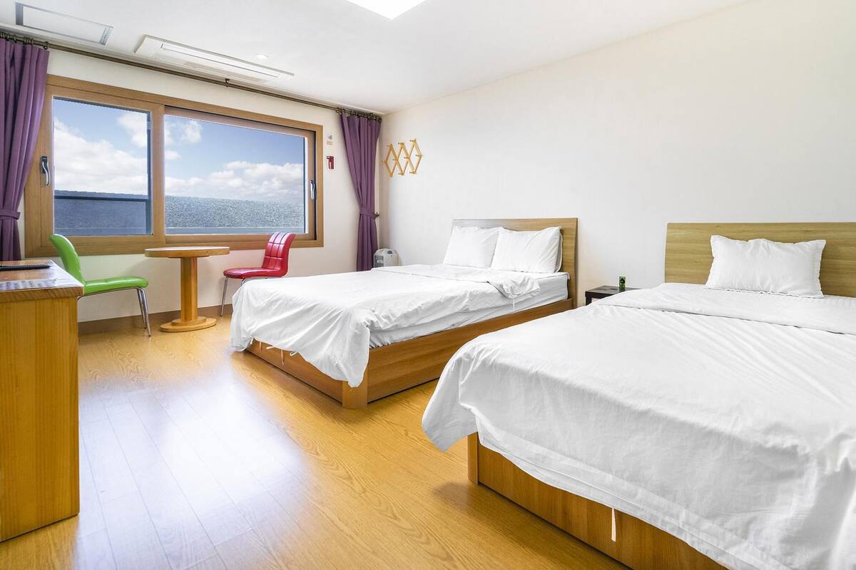 Habitación de hotel con dos camas, un escritorio, una silla y ventana con vistas.