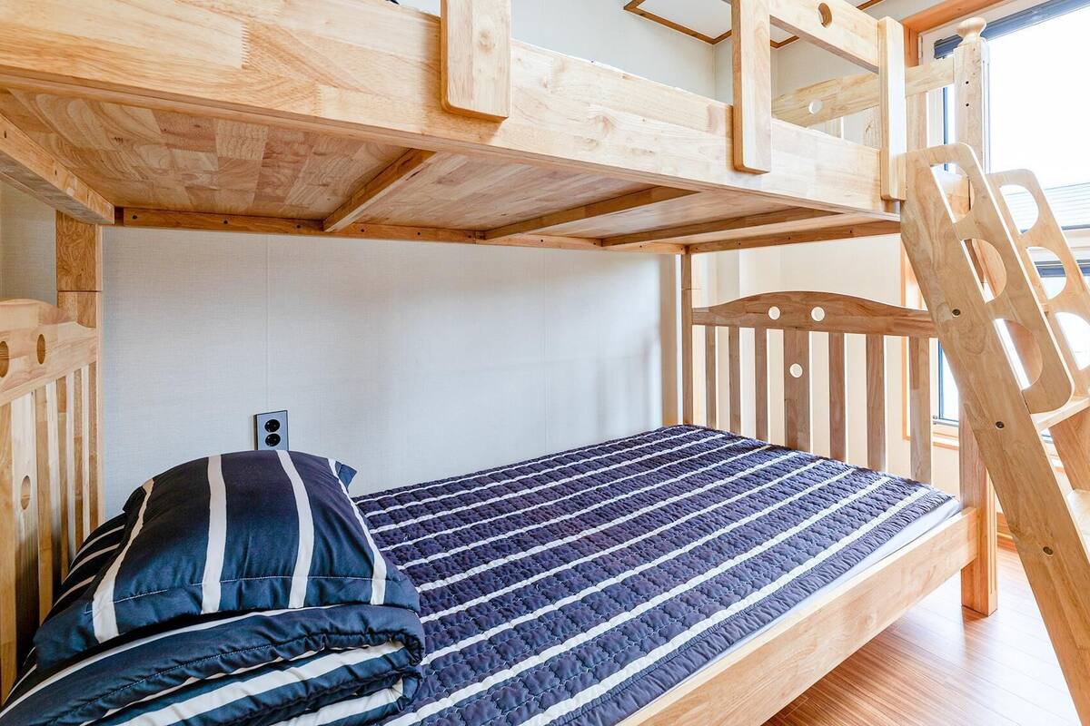 Un lit superposé avec une échelle en bois, un oreiller à rayures et une fenêtre donnant sur un beau paysage.