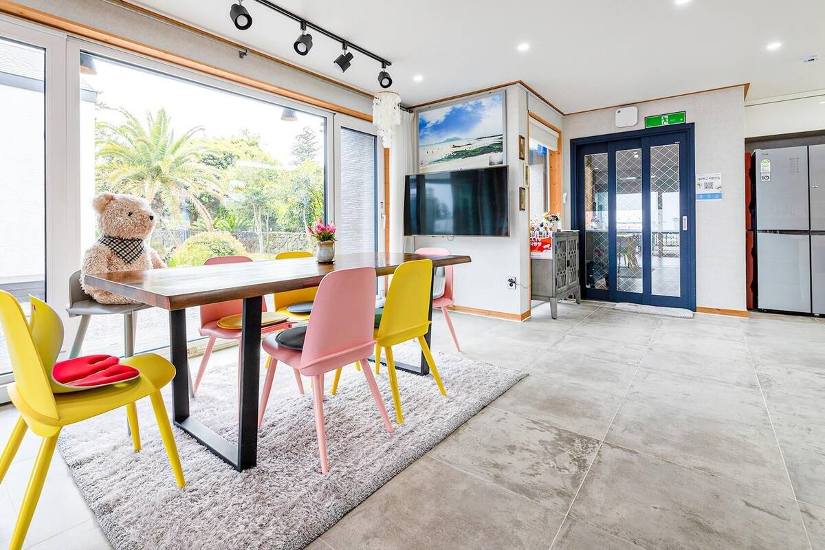 Un espace repas moderne avec une grande table, des chaises colorées et un ours en peluche.