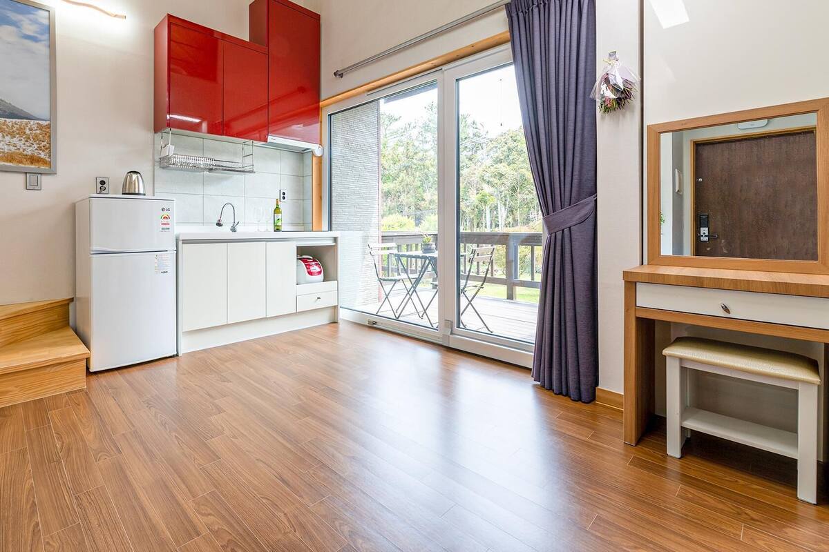 Une cuisine moderne avec des meubles blancs, un meuble supérieur rouge et une grande porte-fenêtre coulissante donnant sur un balcon.