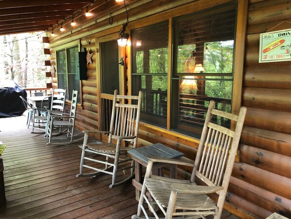 A wooden deck with rocking chairs and a table, overlooking a forested area.